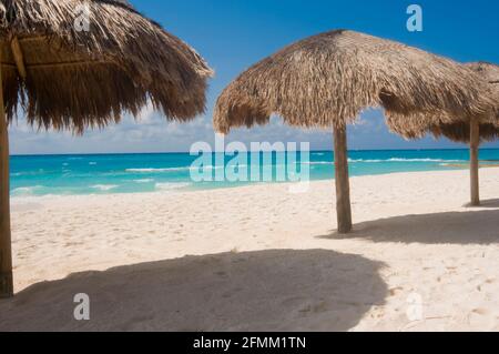 Beach umbrellas made of leaves on a tropical white sand beach facing the sea with blue sky in the background. Stock Photo