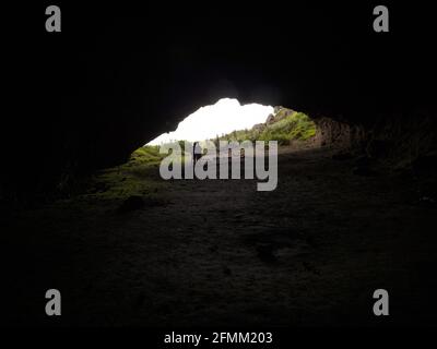 Silhouette of two people standing in black dark rock shelter cavern cave opening mouth at Whatipu Beach Waitakere Ranges West Auckland North Island Ne Stock Photo