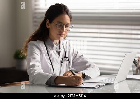 Concentrated hispanic female therapist sit at desk prepare medical report Stock Photo
