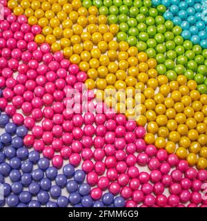 diagonal slant display of round candy coated chocolate sweet treats in purple pink yellow green and blue as studio lighting food scene Stock Photo
