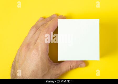 Mans hand holds small white box on yellow background. Copy space. Mock up Stock Photo