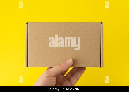 Hand holds rectangular cardboard box, yellow background. Copy space. Mock up Stock Photo