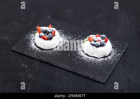 Meringue cakes and fresh berries on black background. Cakes Anna Pavlova Stock Photo