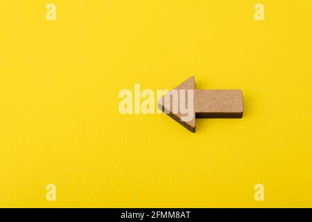 Wooden arrow on yellow background. Direction indicator. Copy space. Mockup. Stock Photo