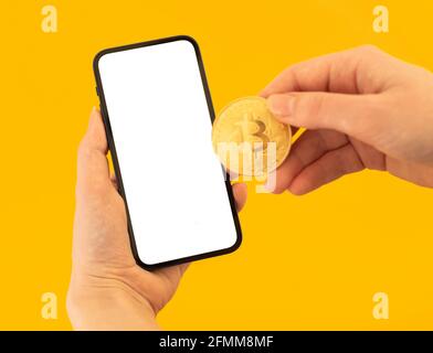 Mockup pay with bitcoin, yellow background, woman with mobile phone and golden coin in hands, copy space photo Stock Photo
