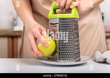 Process of grinding an apple on a grater. Baking ingredients, chef's hands. Stock Photo
