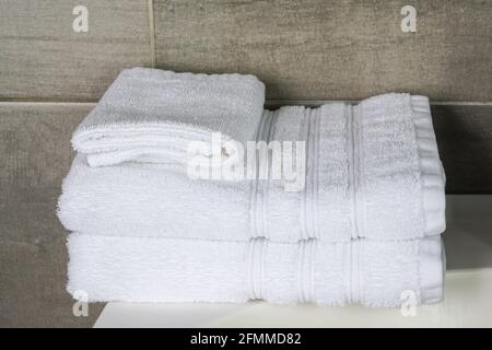 a stack of white clean towels in the hotel bathroom against a gray anthracite tile wall background Stock Photo