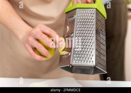 Chef's hands are grating the apple. Preparation of ingredients. Stock Photo