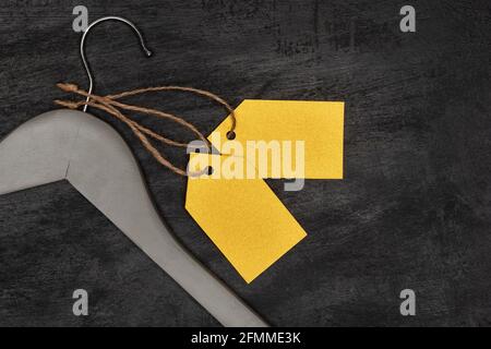 Wooden coat hanger with yellow paper labels, black background. Blank label mockup . Clothing tag. Stock Photo