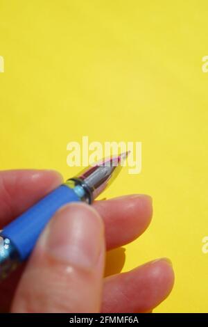 Blue pen in female fingers on yellow paper. Stock Photo