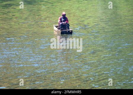 Fisherman sitting huddled in a wooden boat on a pond Stock Photo