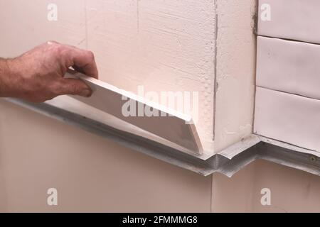 Stylish trendy white ceramic tiles on the kitchen wall. Hands in the process of laying white rectangular tiles on the bathroom wall. Renovation of apa Stock Photo
