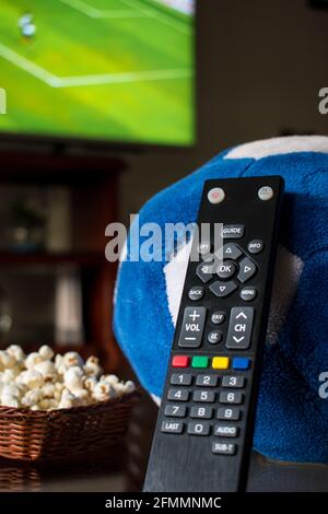 Some pop corn in a basket with a tv control and one soccer ball on a table at home Stock Photo