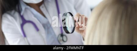 Dermatologist examines patient's face through magnifying glass Stock Photo