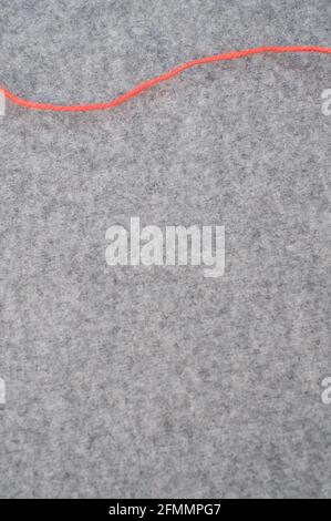 Vertical shot of a loose red piece of string on a gray wool background with copy space Stock Photo