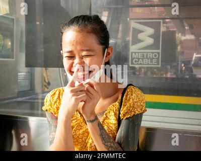 Medellin, Antioquia, Colombia - March 27 2021: Young Asian Woman with a Face Mask under her Mouth is Laughing inside the Cable Car (Metro Cable) Stock Photo