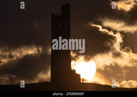 People watch the sun set over Victoria Tower, Castle Hill, Huddersfield. The tower was built to commemorate Queen Victoria's Diamond Jubilee of 1897 however the history of human activity on the Castle Hill dates back over 4000 years Stock Photo