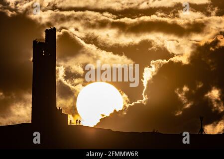 People watch the sun set over Victoria Tower, Castle Hill, Huddersfield. The tower was built to commemorate Queen Victoria's Diamond Jubilee of 1897 however the history of human activity on the Castle Hill dates back over 4000 years Stock Photo
