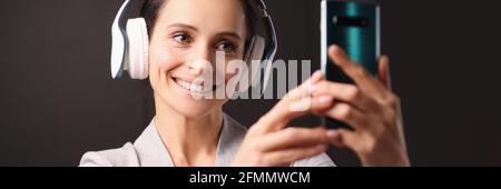 Smiling woman in headphones looks into smartphone Stock Photo