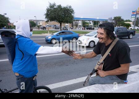 Austin, Texas, USA. 10th May, 2021. Musician and handyman DOUGLAS CRAWFORD, r, greets a street boddy as he strums his guitar for spare change near his camp at the corner of Ben White Blvd. and south Congress Avenue in Austin, TX where he's lived for over a year. Crawford, 60, says he stays to himself and isn't worried about Austin's new homeless crackdown and camping ban starting Tuesday. Credit: Bob Daemmrich/ZUMA Wire/Alamy Live News Stock Photo