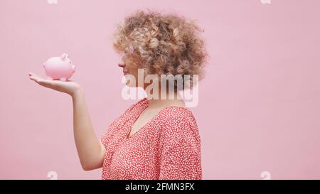 Woman holding small piggy bank in her hand and making funny faces. Big expectation small investment growth. High quality photo Stock Photo
