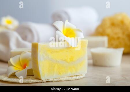 Handmade soap, spa bath products white towels tropical plumeria flowers on marble table in bathroom. Eco beauty cosmetic for wellness health skincare. Stock Photo