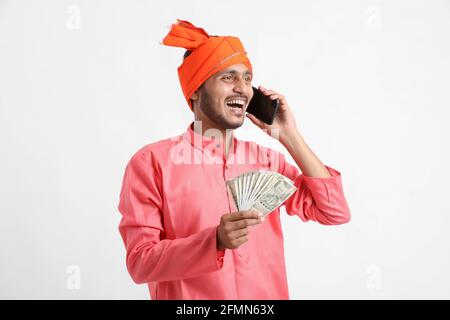 Young indian farmer talking on mobile phone and showing money on white background. Stock Photo
