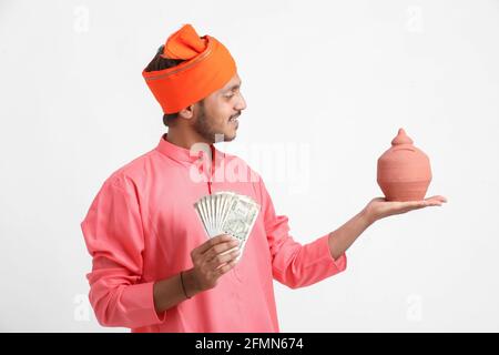 Indian farmer holding clay piggy bank and currency in hand on white background. Stock Photo