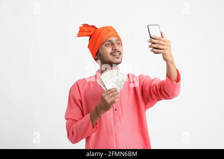 Young indian farmer using smartphone and showing money on white background. Stock Photo