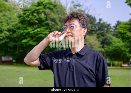 Middle-aged Asian man using nasal spray outdoors. Stock Photo