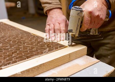 Carpenter puts together planks on the door frame using a pneumatic stapler in the carpentry workshop. Stock Photo