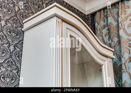 Classical style white showcase with glass doors and gilding on the background of black and white wallpaper with floral pattern closeup view Stock Photo