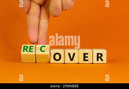 Time to recover symbol. Businessman turns wooden cubes and changes the word 'over' to 'recover'. Beautiful orange table, orange background. Business, Stock Photo