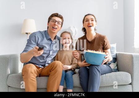 Happy family watching TV with popcorn  at home. Mother, father and daughters spending time together. Stock Photo