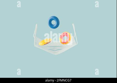 Creative layout with swimming inflatable circles and medical mask on a blue background. Concept of safety from CoronaVirusor symbol of lost summer. Stock Photo