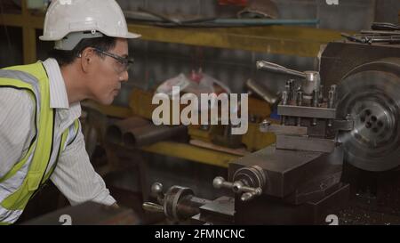 Asian professional mechanical engineer or operation man wearing uniform goggles safety working on workshop metal lathe industrial manufacturing factor Stock Photo