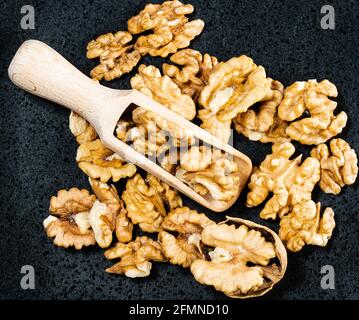 top view of wooden scoop in heap of peeled walnuts on black plate Stock Photo