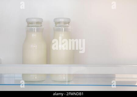 Dairy products in glass bottles on shelf of open empty fridge. White milk in  refrigerator. Horizontal view with copy space. Stock Photo