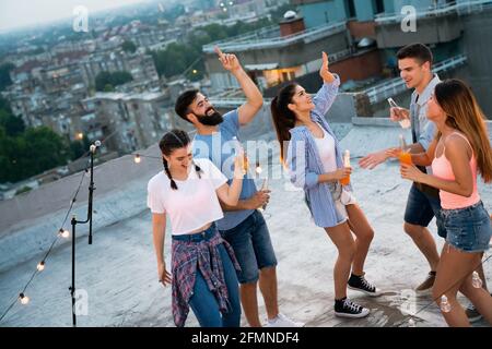 Friends enjoying cocktails at a party. Group of happy people having fun, dancing on a rooftop Stock Photo