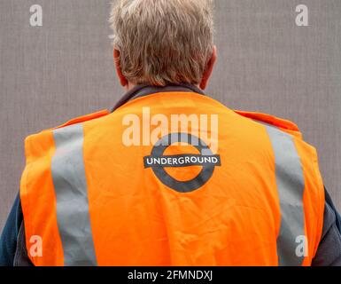 Close POV shot of the back of an older man, indoors, wearing an orange London Underground hi viz safety vest. Stock Photo