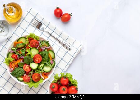 Vegetables on a white plate on a gray marble background. Top view. Salad made with cherry tomatoes, cucumbers, arugula, basil and dressed with olive o Stock Photo