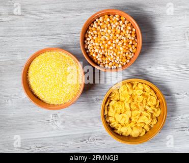 top view of maize corns, cornmeal and cornflakes in round ceramic bowls on gray wooden table Stock Photo