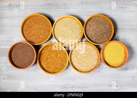 top view of various millet seeds in round ceramic bowls on gray wooden table Stock Photo