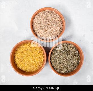 top view of various precooked wheat groats (crushed wheat, freekeh, bulgur) in round ceramic bowls on gray concrete board Stock Photo