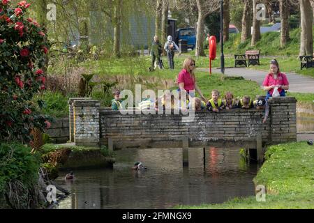 A group of young children from a pre-school nursery supervised by their nursery workers looking over a small footbridge at the ducks in Trenance Garde Stock Photo