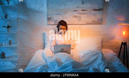 Woman in pajama using laptop in bedroom during night Stock Photo