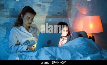 Freelancer using laptop near daughter with digital tablet on bed Stock Photo