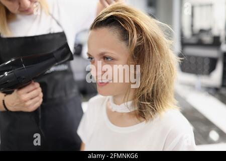 Hairdresser drying hair with hairdryer to woman in barber shop Stock Photo
