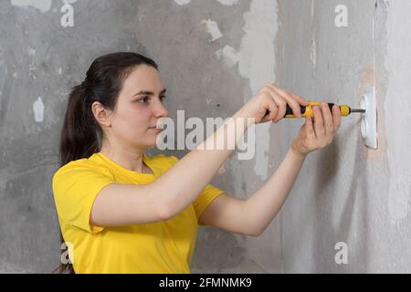 A woman repairman unscrews a screwdriver socket. Repairs in the house on their own. Fixing electrical grids Stock Photo