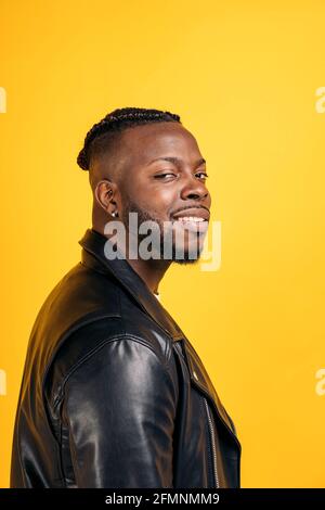 Confident black man wearing black leather jacket smiling and looking at camera in studio shot. Stock Photo